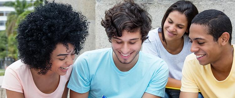 Grupo de jóvenes adultos sonriendo y mirando juntos un objeto.