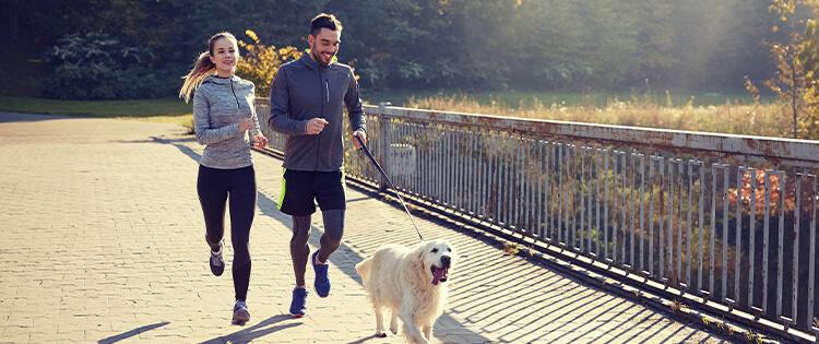 Un hombre y una mujer trotando con un perro.