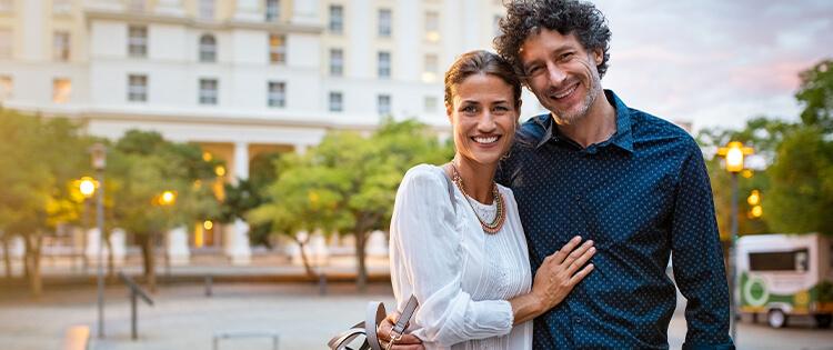 Una pareja parada frente a un edificio posando juntos hacia a la cámara.