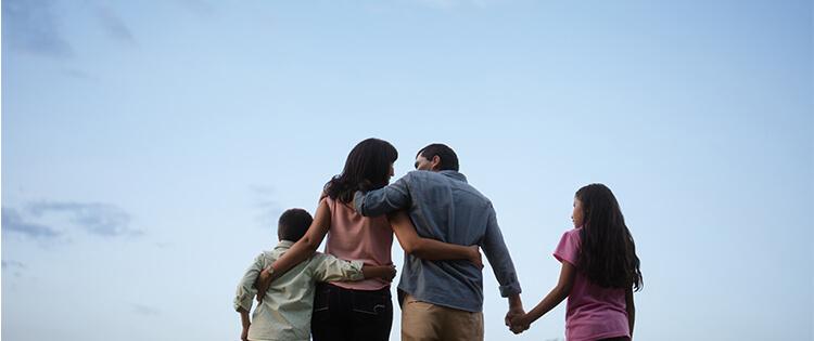 Una familia de espaldas está abrazado mirando hacia el cielo.