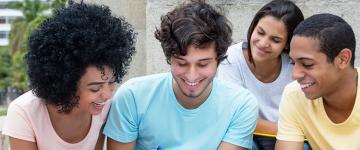 Grupo de jóvenes adultos sonriendo y mirando juntos un objeto.