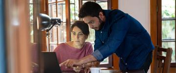 Un hombre y una mujer frente a un computador. El hombre señala algo en la pantalla.