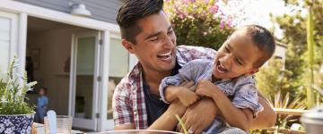 Un padre en el jardín jugando y riendo con su hijo.