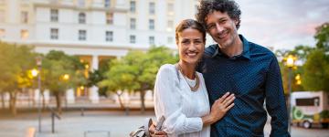 Una pareja parada frente a un edificio posando juntos hacia a la cámara.