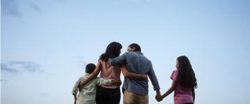 Una familia de espaldas está abrazado mirando hacia el cielo.