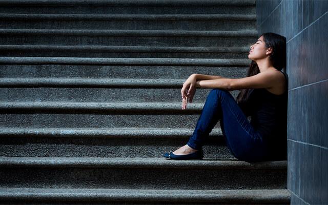 Una mujer sentada en las escaleras recostada contra la pared, con sus ojos cerrados.
