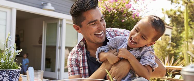 Un padre en el jardín jugando y riendo con su hijo.